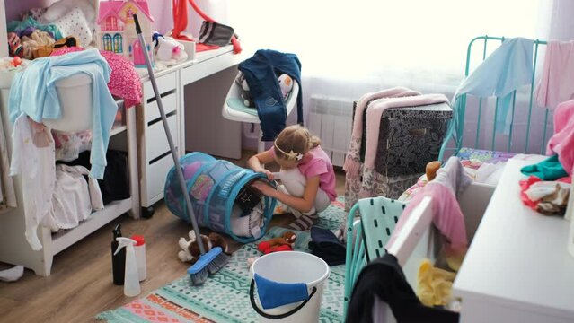 Little girl putting scattered toys in the basket in her messy room, slow motion