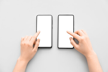 Female hands with modern mobile phones on light background