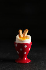 Holder with soft boiled egg and croutons on black background