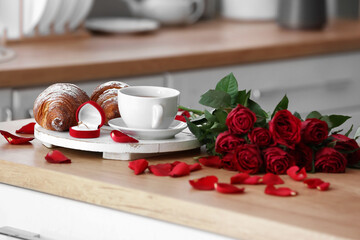 Tray with engagement ring, cup of tea, croissants and roses on counter in kitchen, closeup