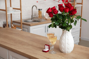 Engagement ring, vase with roses and glasses of champagne on counter in kitchen decorated for Valentine's Day