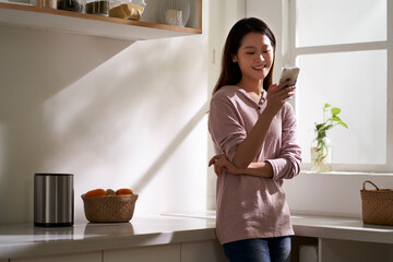 young asian woman using mobile phone in kitchen at home