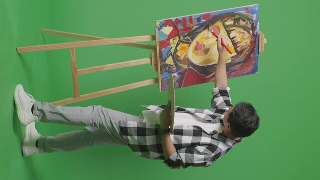 Full Body Side View Of Asian Male Artist Celebrating Finish Painting A Girl On The Canvas By Oil Paints And Brush In The Green Screen Studio
