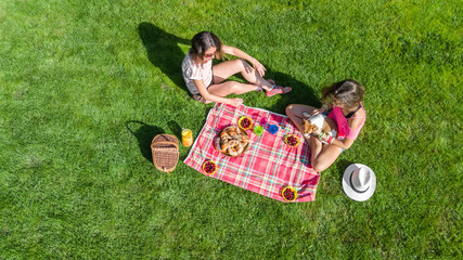 Friends having picnic in park, young girls with dog relaxing on grass and eating healthy food...