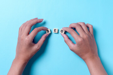 Hands arrange SEO word on wooden cube on blue background. Search Engine Optimization concept.