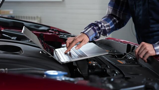 Woman auto mechanic doing engine diagnostics using laptop. 