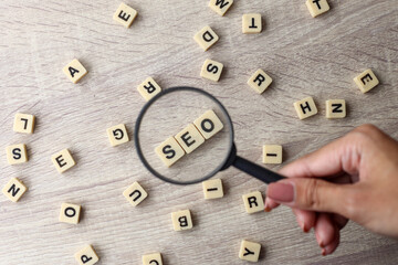 Selective focus of magnifying glass and written with SEO, Search Engine Optimization on a wooden background.