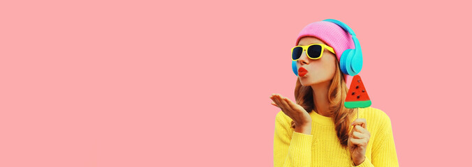 Summer colorful portrait of young woman in headphones listening to music with fruit juicy lollipop or ice cream shaped slice of watermelon on pink background, blank copy space for advertising text
