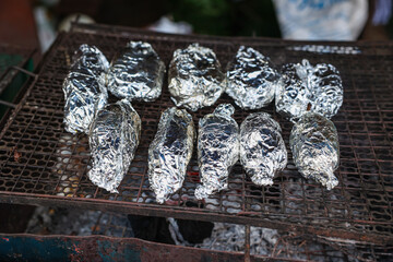 fish or potato wrapped covering with aluminium foil paper grilling on charcoal stove