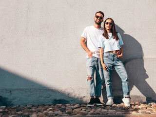 Smiling beautiful woman and her handsome boyfriend. Woman in casual summer jeans clothes. Happy cheerful family. Female having fun. Sexy couple posing in street at sunny day. Near wall. Full length