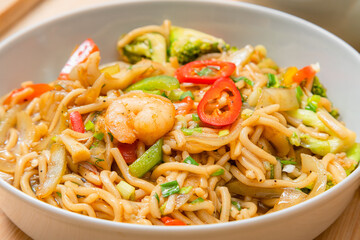 Golden coloured spicy sea food noodles with shrimp, broccoli, chilli pepper in a plate on wooden table