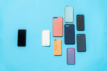 Pile of multicolored plastic back covers for mobile phones on blue background with a phone on the side