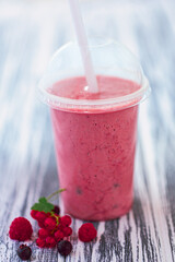 Closeup berries milkshake in plastic cup with ingredients on wooden background. Selective focus 