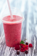 Closeup shot berries milkshake in plastic cup with ingredients on wooden background. Selective focus