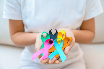World cancer day, February 4. Hand holding blue, orange, teal, pink, black and yellow ribbons for supporting people living and illness. Healthcare and Autism awareness day concept