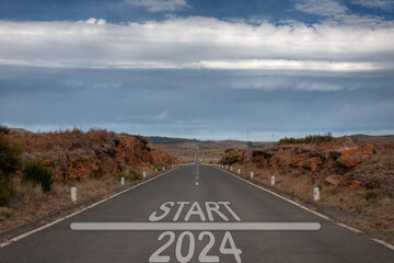 Start 2024 year road sign on a country road with wind electricity plants in the background as a concept of renewable energy friendly year - 558070105