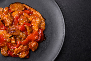 .Delicious juicy meat with hot peppers and sauce on a black ceramic plate