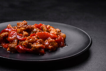.Delicious juicy meat with hot peppers and sauce on a black ceramic plate