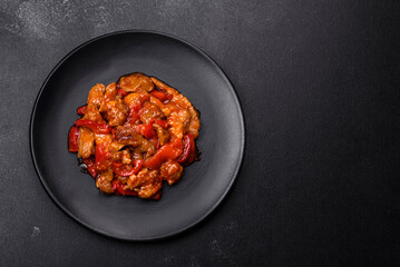 .Delicious juicy meat with hot peppers and sauce on a black ceramic plate