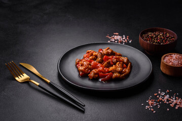 .Delicious juicy meat with hot peppers and sauce on a black ceramic plate