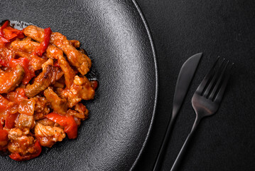 .Delicious juicy meat with hot peppers and sauce on a black ceramic plate