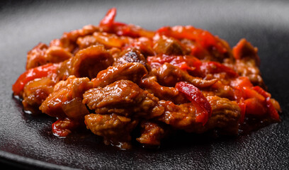 .Delicious juicy meat with hot peppers and sauce on a black ceramic plate