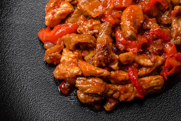 .Delicious juicy meat with hot peppers and sauce on a black ceramic plate