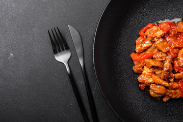 .Delicious juicy meat with hot peppers and sauce on a black ceramic plate