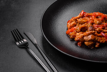 .Delicious juicy meat with hot peppers and sauce on a black ceramic plate
