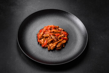 .Delicious juicy meat with hot peppers and sauce on a black ceramic plate