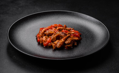 .Delicious juicy meat with hot peppers and sauce on a black ceramic plate