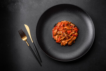 .Delicious juicy meat with hot peppers and sauce on a black ceramic plate
