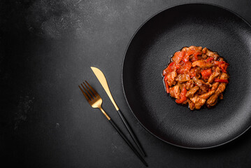 .Delicious juicy meat with hot peppers and sauce on a black ceramic plate
