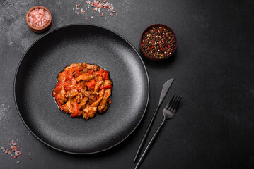 .Delicious juicy meat with hot peppers and sauce on a black ceramic plate
