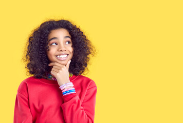Fototapeta na wymiar Pensive smiling African American girl isolated on yellow studio background look at copy space aside. Happy biracial teen child consider good sale deal or promotion offer. Advertising concept.