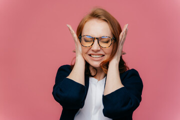 Stressed female teacher covers ears, has headache because of noisy pupils, clenches teeth, ignores noise, wears optical glasses, formal clothes, poses against pink background. Facial expressions