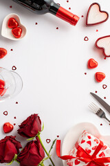 Valentine's Day concept. Top view vertical photo of wine bottle wineglass roses giftbox heart shaped saucer candies cutlery candles confetti on isolated white background with empty space in the middle