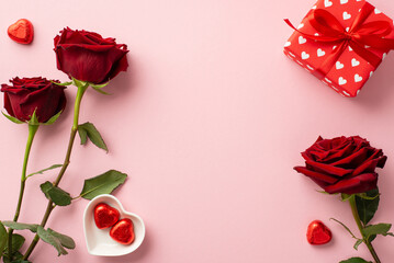 Valentine's Day concept. Top view photo of red roses heart shaped saucer with chocolate candies and present box on isolated pastel pink background with empty space