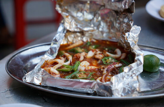 Squid cooked with spicy sauce in aluminium foil paper served on the street of Kuala Lumpur                                                             