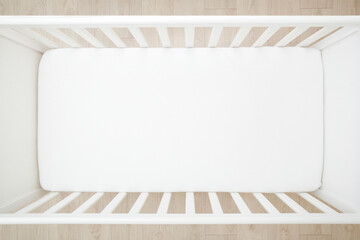Empty baby crib with white mattress on wooden home floor. Closeup. Top down view. - Powered by Adobe
