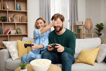 Obraz na płótnie Canvas Happy Couple Playing Video Games. Boyfriend And Girlfriend Sitting On Couch In Living Room Enjoying Playing Video Games And Spending Time Together. Happy Girl Closed Eyes Of Guy