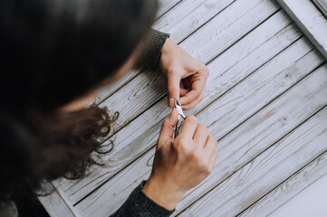 Hands of a woman, a girl close-up, making herself a manicure, cutting cuticles with special scissors on fingers, nails on a wooden white background. Close-up photography, work, beauty, art.