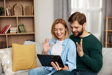 Fototapeta na wymiar Couple Talking Tablet At Home. Young Couple Using Digital Tablet While Sitting On Couch. Happy Smiling People Watching Video On Digital Tablet At Home 