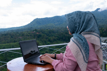 Asian woman wearing hijab enjoys freelance work on her laptop on vacation. freelance or digital nomad concept