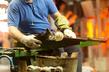 A glass blower is working on the manufacture of glass vases and glasses.