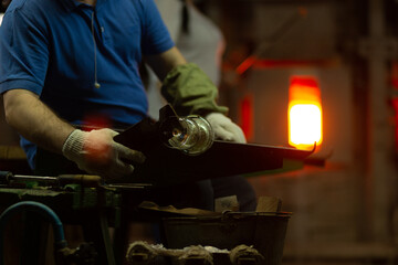 A glass blower is working on the manufacture of glass vases and glasses.