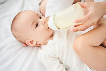 Obraz na płótnie Canvas Cute little newborn boy eats milk from a bottle, a nipple.