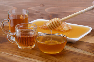 a bowl of honey with honey dipper, glass cup of tea, and honeycomb on wooden table