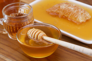 a bowl of honey with honey dipper, glass cup of tea, and honeycomb on wooden table