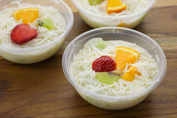 selective focus creamy fruit salad served in plastic bowl on wooden background